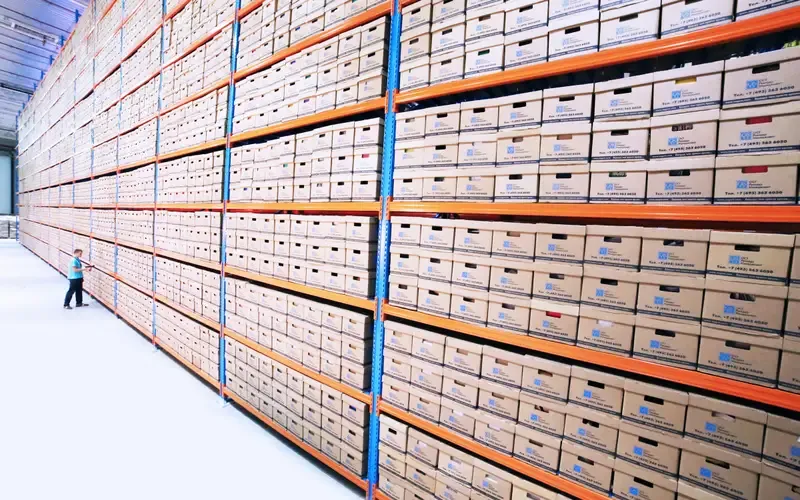 Rows of numbered archive boxes on warehouse shelving, receding into the distance